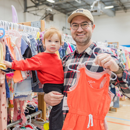 A mom and grandmother stand beside a rack of clothing at a JBF sale in Texas.